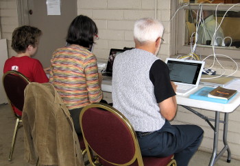 Three members complete the questionnaire on the laptops set up outside the office.